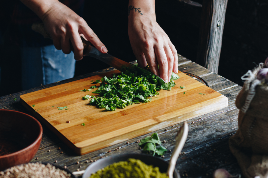 A closely cropped photograph of a person chopping fresh herbs on a wooden chopping board