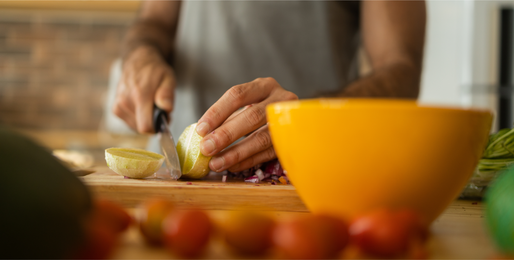 A person slicing fruit on a wooden cutting board in a warmly lit kitchen