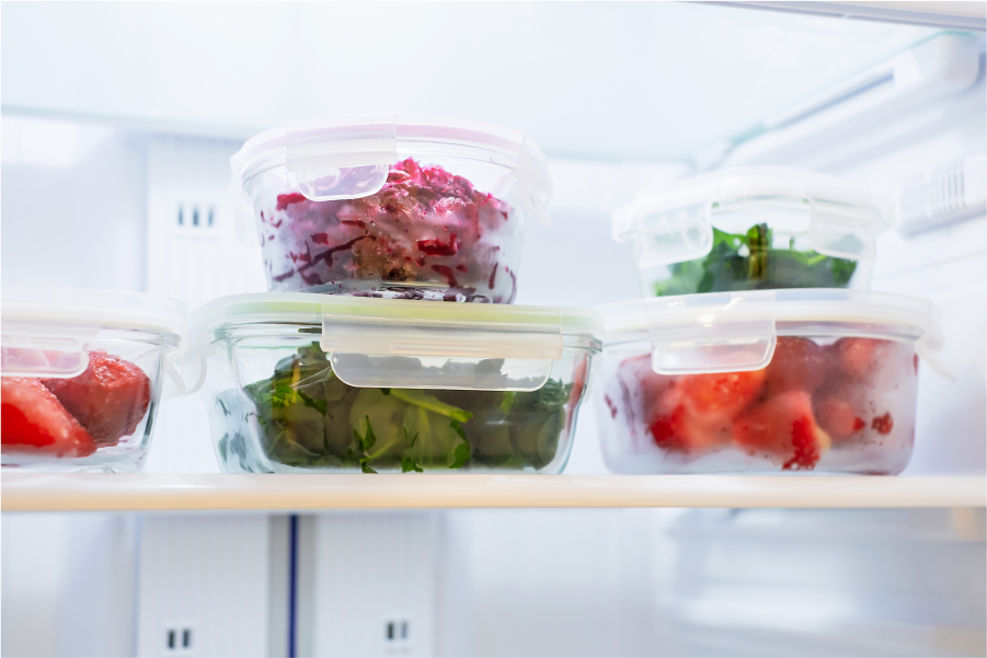 An assortment of clear plastic containers containing prepared vegetables neatly arranged in a refrigerator shelf