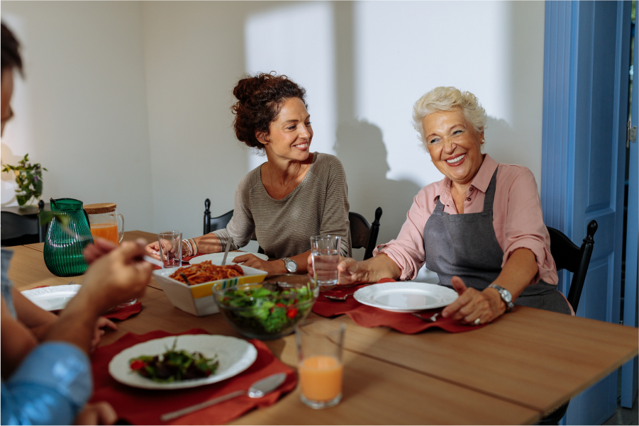 A family sitting at table which has serving dishes containing pasta and salad in the centre of it.