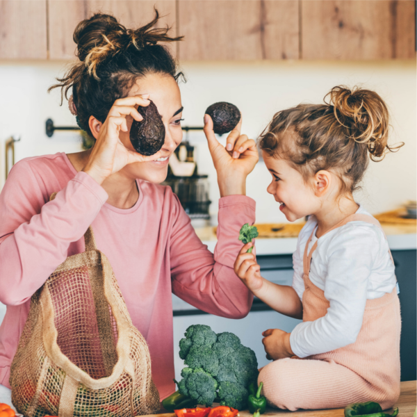 A woman and young girl in the kitchen, the woman is entertaining the child with two avocados