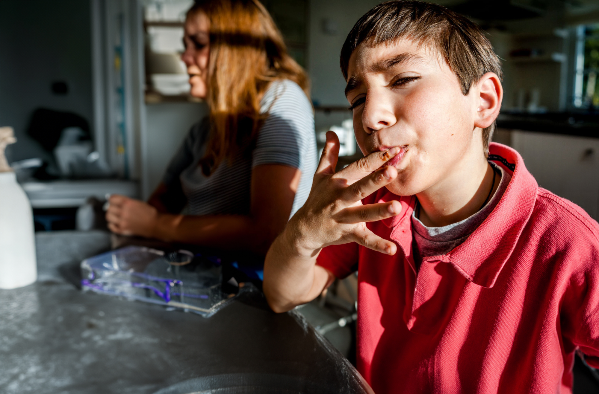 A child sitting at the table, licking sauce from his fingers