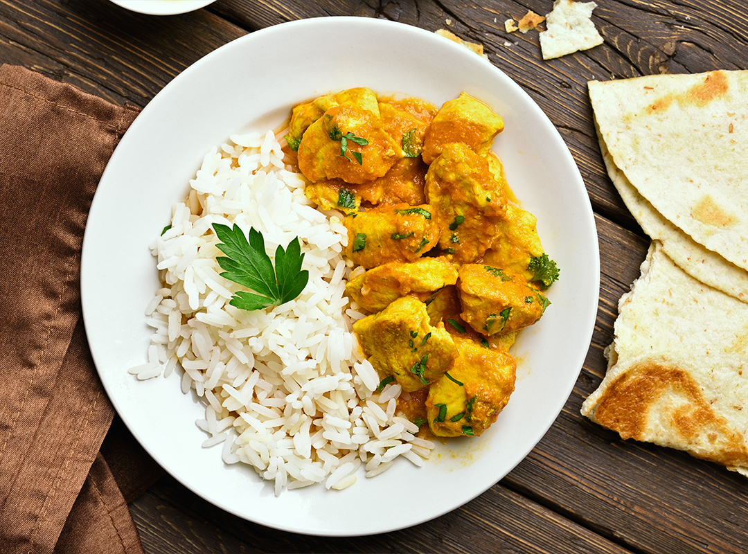 Bowl of creamy coconut curry and chicken sitting on a table with naan