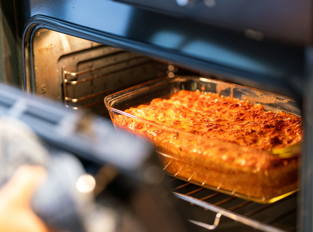 Lasagna sitting in an oven cooking with the door slightly open