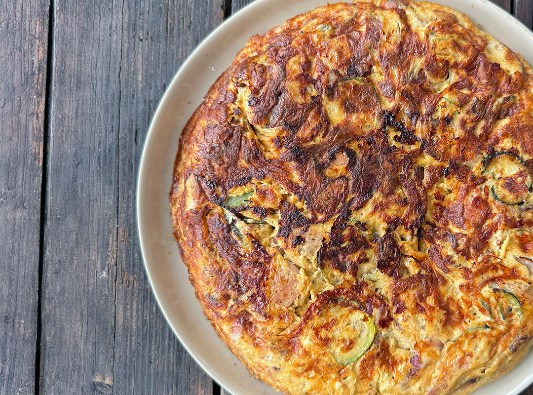 Top view of a Cheesy Baked Pasta Frittata sitting on a plate on a timber table