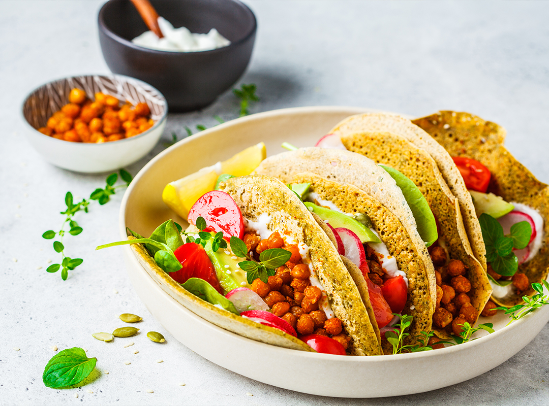 Three tacos sitting in a bowl with chickpeas in a small bowl in the background
